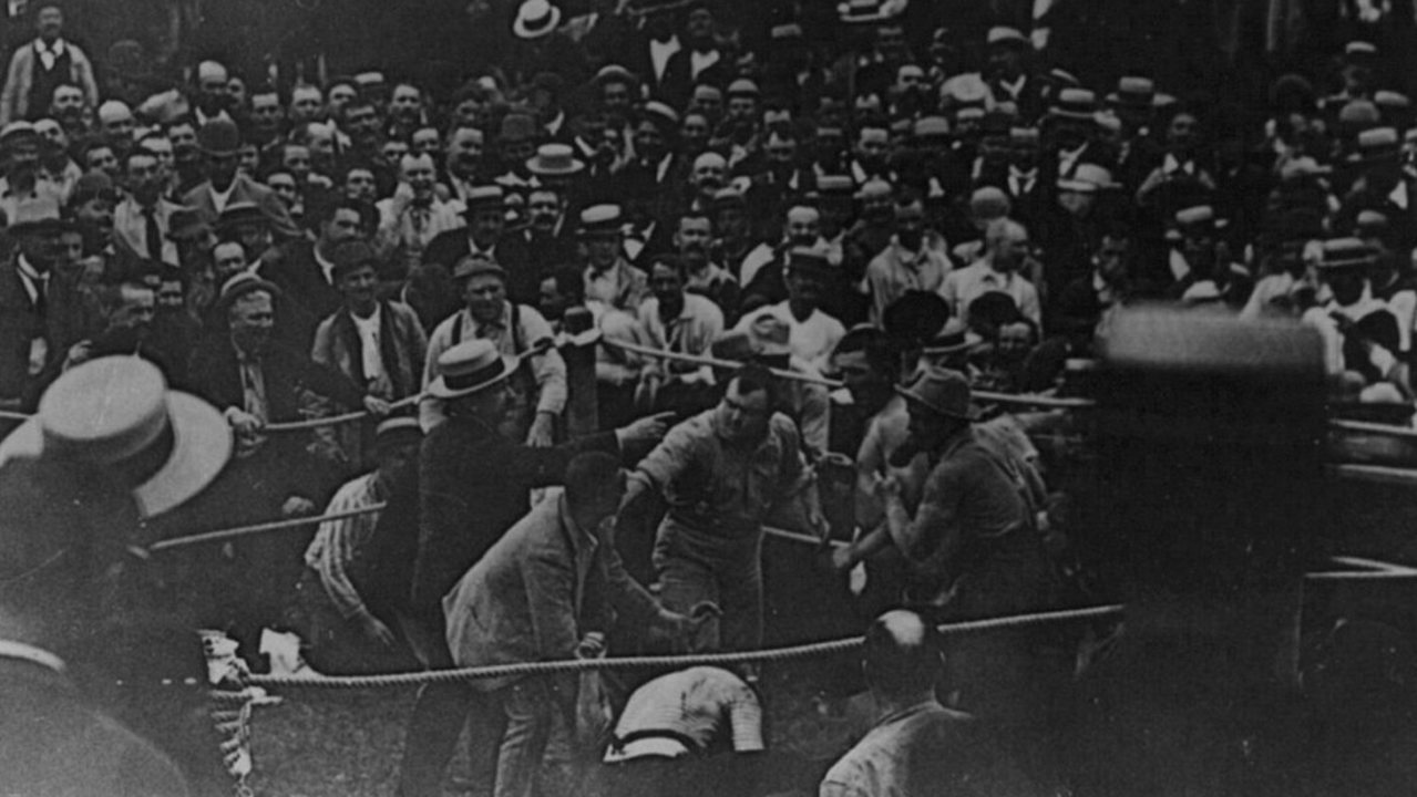 ภาพถ่ายขาวดำปี 1889 ฝูงชนสวมหมวกยืนล้อมเวทีมวยกลางแจ้งในรัฐมิสซิสซิปปี ดูการชกหมัดเปล่าระหว่างจอห์น แอล. ซัลลิแวน กับเจค คิลเรน