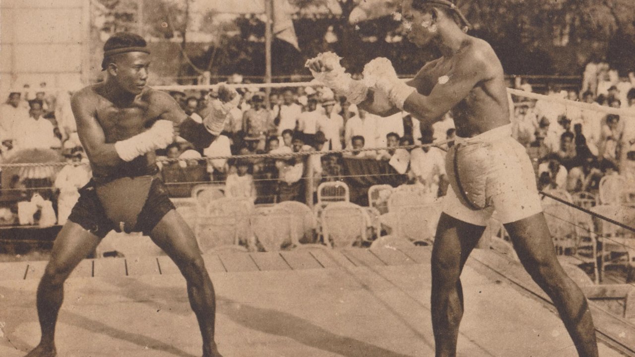 ภาพถ่ายเก่าการชกมวยไทยกลางแจ้งในกรุงเทพฯ ยุค 1920 มีผู้ชมยืนล้อมรอบสังเวียน
