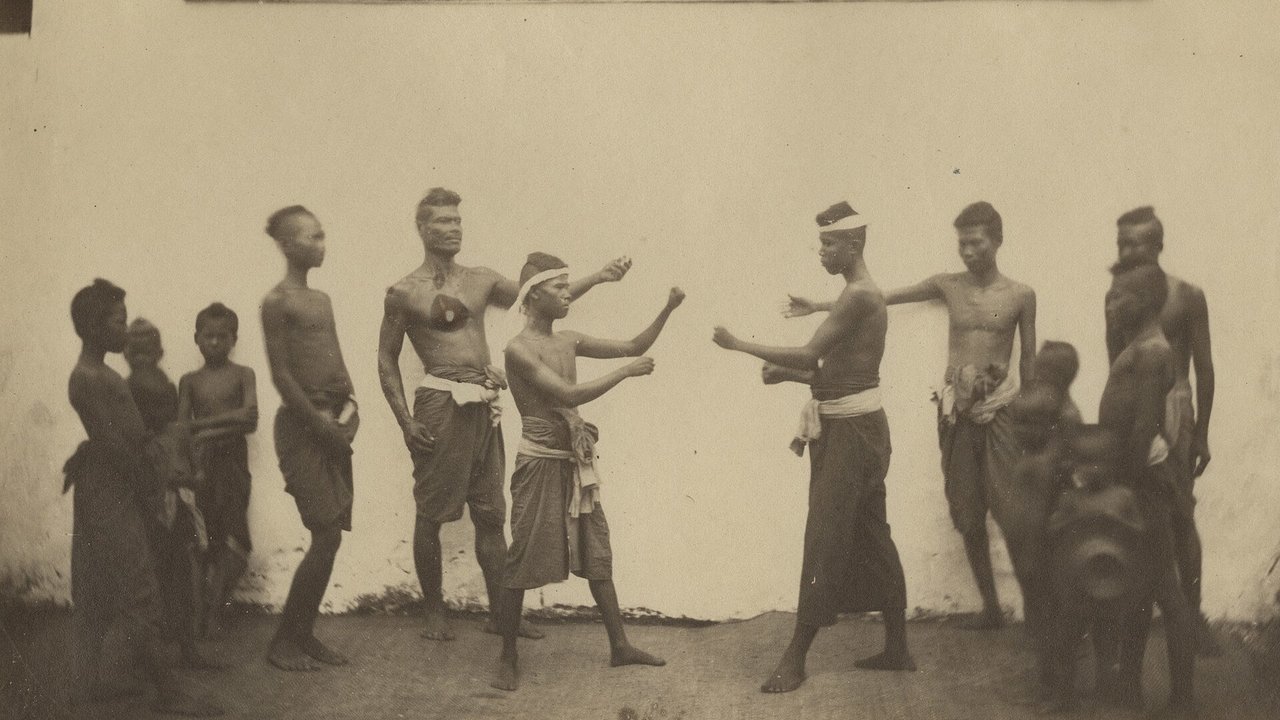 ภาพถ่ายขาวดำปี 1865 นักมวยสยามสองคนตั้งท่าชกกันกลางลาน โดยมีผู้ชมยืนล้อมดูอยู่สองข้าง