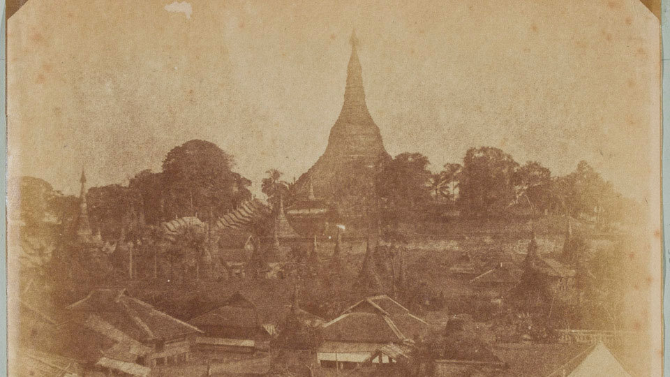 ภาพถ่ายเก่าสีซีเปียปี 1852 มหาเจดีย์ชเวดากองตั้งตระหง่านอยู่เหนือหมู่บ้านและต้นไม้ในเมืองย่างกุ้ง